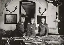 Photographie de trois hommes en uniforme militaire penchés sur des cartes géographiques.