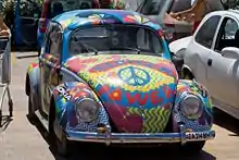 Photographie d'une Volkswagen Coccinelle couverte de dessins hippies dont des fleurs et des couleurs vives.