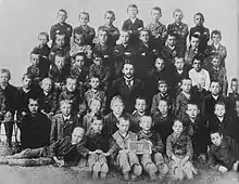Photo de classe noir et blanc d'une cinquantaine de garçons réunis autour de leur maître d'école ; le jeune Hitler se tient debout, au centre de la rangée supérieure.