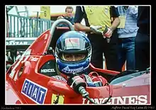 Photographie d'un pilote casqué, vu de face, dans sa monoplace de Formule 1 rouge, en gros plan.