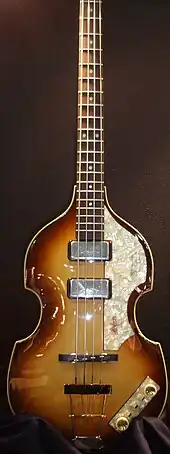 Photographie en couleur d'un instrument de musique à quatre cordes disposé verticalement.