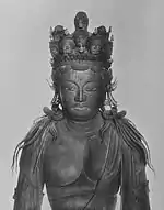 Frontal view of the head of a sculpture of a deity. A number of small heads and small statues are placed on top of the head.
