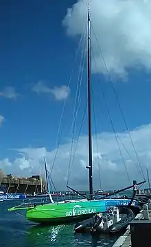 Vu de trois quarts avant, en entier, voilier vert et bleu amarré à un ponton.