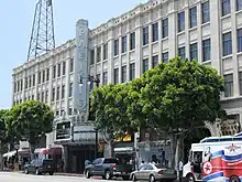 Un bâtiment blanc qui comporte beaucoup de fenêtres. Un grand panneau vertical se trouve au milieu de la façade sur lequel on peut lire Pacific. Plusieurs voitures sont arrêtées le long de la route devant le bâtiment.