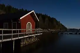Lumière de lune sur un club de bateaux à Lysekil (commune), Suède. Dans le fond, les lumières de la route européenne 6. Novembre 2017.