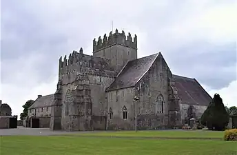 Photographie d'une église en pierres massive surmontée d'une tour-clocher crénelée.