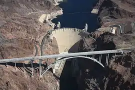 Vue aérienne d'un pont suspendu entre deux terres séparées par un cours d'eau arrêté par un barrage.