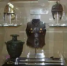 Armure de bronze d'un hoplite, avec des inserts dorés sur la poitrine. Le casque en haut à gauche est une version restaurée du casque oxydé à droite.