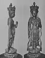 Vue de face et de profil d'une statue debout avec son bras gauche plié en avant. Sur la tête il y a de petites têtes orientées dans des directions différentes.
