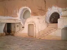 Photo d'une maison taillée dans la roche avec des soubassements blancs.