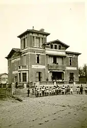 Photo noir et blanc d'une grande villa en bord de mer, vue de la plage, avec un groupe d'enfants.