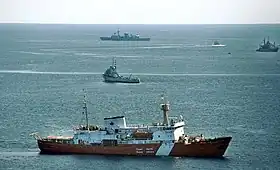 Photo couleur. Quatre navires navigants, avec au premier plan de profil une coque rouge à bande blanche surmontée d'une superstructure banche.