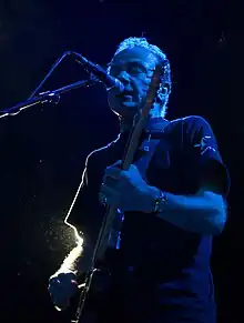 un homme qui joue de la guitare devant un micro dans la nuit.