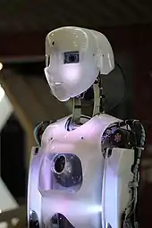 Robot humanoïde blanc de profil, éclairé d'une lumière légèrement violette.