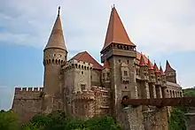 Photographie en couleurs d'un château aux remparts crénelés et aux nombreux donjons, relié à la terre par un seul pont.