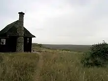 a large wooden hut with a stone chimney, standing in a grassy landscape