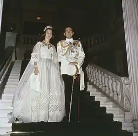 Photographie en couleur montrant une femme en robe de mariée et un homme en uniforme de marine dans un escalier.