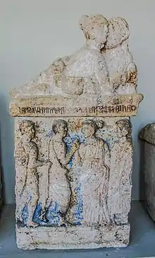 Sculpture en pierre d'un couple enlacé, sous lequel apparaissent quatre personnages en bas-relief.