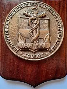 Plaque de bronze sur bois présentant l'insigne de l'institut