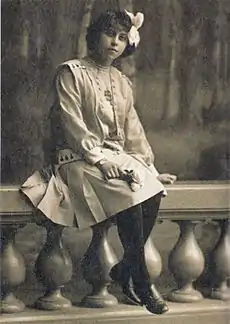 Photographie sépia d'une jeune fille en pied assise sur le rebord d'une balustrade.