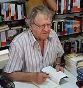 Photo de Ian Gibson assis à un bureau avec un livre à la main, devant des rayonnages de livres.