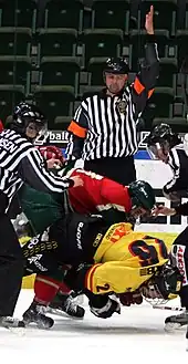 Photo de deux joueurs qui se battent devant un arbitre qui lève le bras en signe de pénalité.