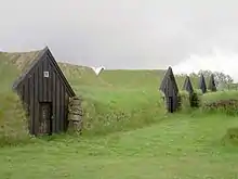 Photographie de maisons islandaises médiévales, en bois, incrustées dans des mottes de terre.