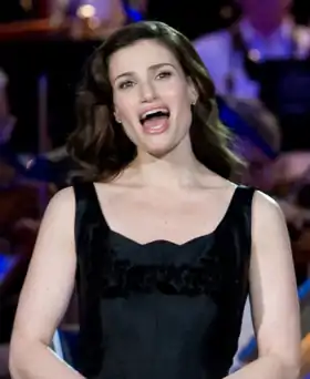 Femme brune portant une robe noire sans manches, la bouche grande ouverte en train de chanter