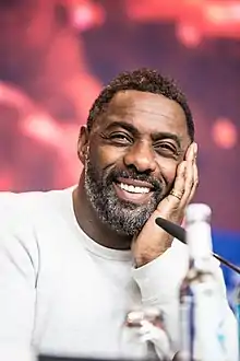 Photo montrant la tête et le buste d'Idris Elba, souriant et portant un pull blanc.