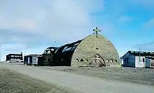 Église de pierres en forme de demi-cercle avec une grande porte en bois et une croix sur la façade.