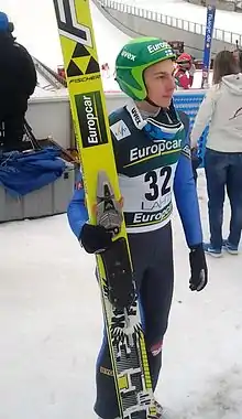 Un homme vu de face, tenant une paire de skis.
