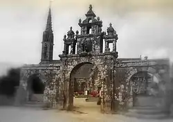 Photo floutée moitié en noir et blanc et moitié en couleur représentant un arc de triomphe en granit devant une église.