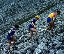  Trois coureurs grimpant dans un pierrier, les mains posées sur les cuisses.