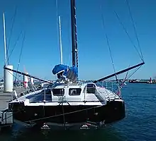 Le bateau vu de l'arrière. Rouf et pont blancs. Tableau arrière noir. Conception singulière : le rouf se prolonge jusqu'à l'arrière du bateau, et sa partie arrière est aussi haute que sa partie avant, mais nettement plus étroite.