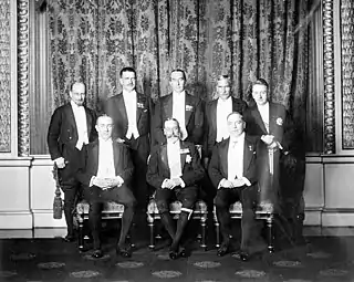 Groupe de huit hommes en costume de soirée. Le roi est assis au milieu entouré par ses premiers ministres.