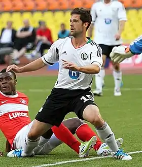 Photographie d'un footballeur de trois-quarts, dans son ensemble, avec un maillot blanc et un short noir.