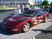 Photographie en couleur d'une voiture de sport bordeaux, vue de trois-quarts, à l'arrêt, exposée à l'extérieur sous le soleil.