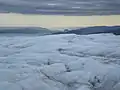 La terre, à l'horizon, est à plusieurs dizaines de kilomètres. Les notions de distances sont bouleversées. La petite colline au centre peu avant l'horizon est le pain de sucre de Kangerlussuaq.