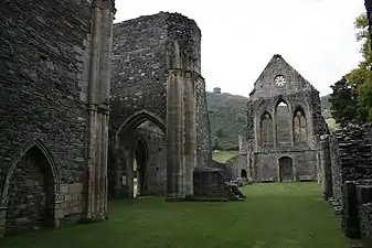 Photographie d'une nef ruinée d'église, bordée de bas-côtés mieux préservés, et se terminant par un pignon à peu près intact.