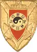 Insigne régimentaire du 10e Régiment d’Artillerie de Marine. Symbole ying -yang or et noir sur écu rouge brochant sur canons croisés et ancre le tout sur écu.