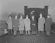 Photographie noir et blanc de sept hommes avec manteaux et chapeaux presque tous identiques.