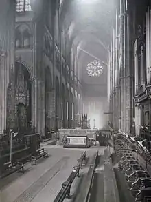 Photographie en noir et blanc de l'intérieur d’une cathédrale, au chœur bordé de deux rangs de stalles de chaque côté.