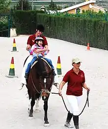 Un enfant tenu par un adulte sur le dos d'un cheval.