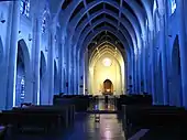 Photographie couleur d'une nef d'église dont les ogives bleutées sont en béton.