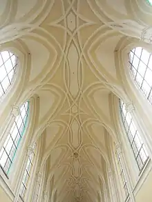 Photographie couleur de la voûte d'une grande église, dont les nervures se croisent en formant des motifs courbes.