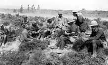 Photographie de plusieurs soldats portant des uniformes différents accroupis dans un paysage de maquis