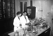 photographie en noir et blanc d'Irène et Frédéric Joliot-Curie en blouse blanche en train de travailler dans un laboratoire