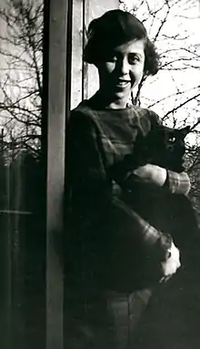 Photo en noir et blanc d'une jeune femme souriante avec une masse de cheveux sombres et un gros chat noir dans les bras.