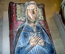 Photographie d'une tombe médiévale avec le gisant d'une femme les mains en croix au-dessus d'une robe bleue.