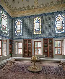 salle décorée de carrelage bleu ; trois arches ; des divans au sol